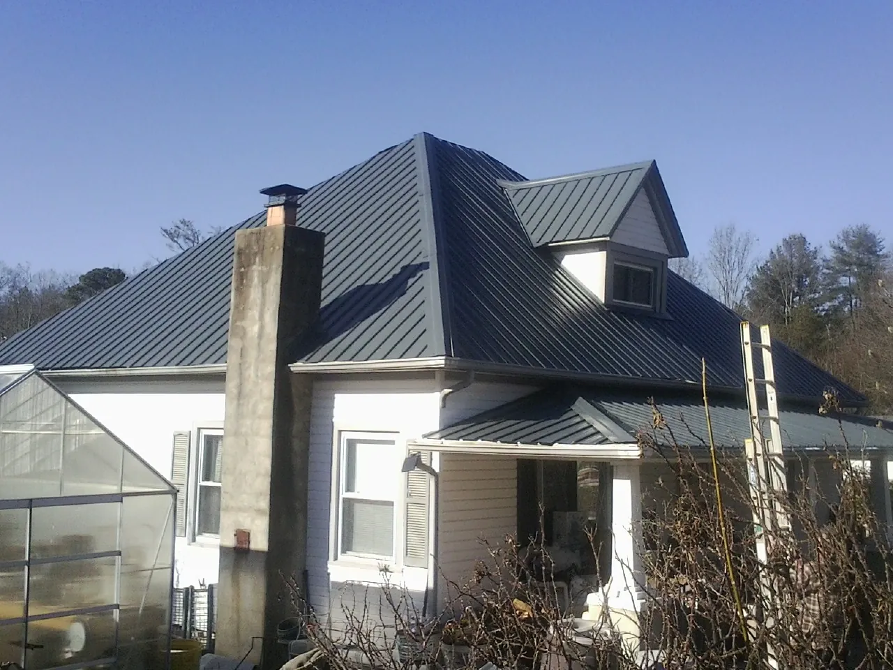 Dark blue standing seam metal roof on a white farmhouse with dormer in La Vergne