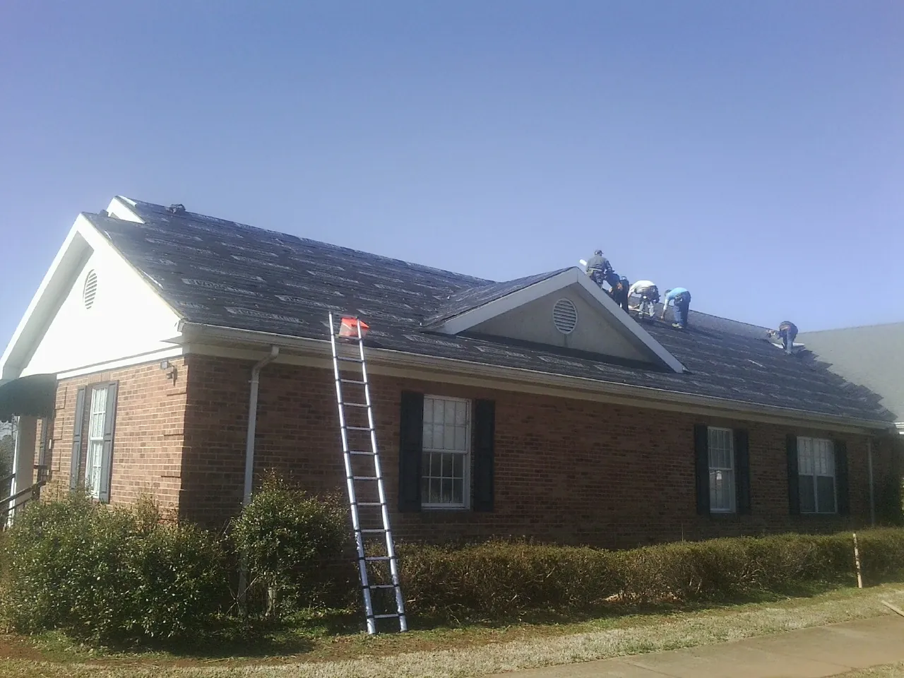 Crew tearing shingles off a brick ranch roof with a ladder set — Emergency Roof Repair work by our crew in La Vergne
