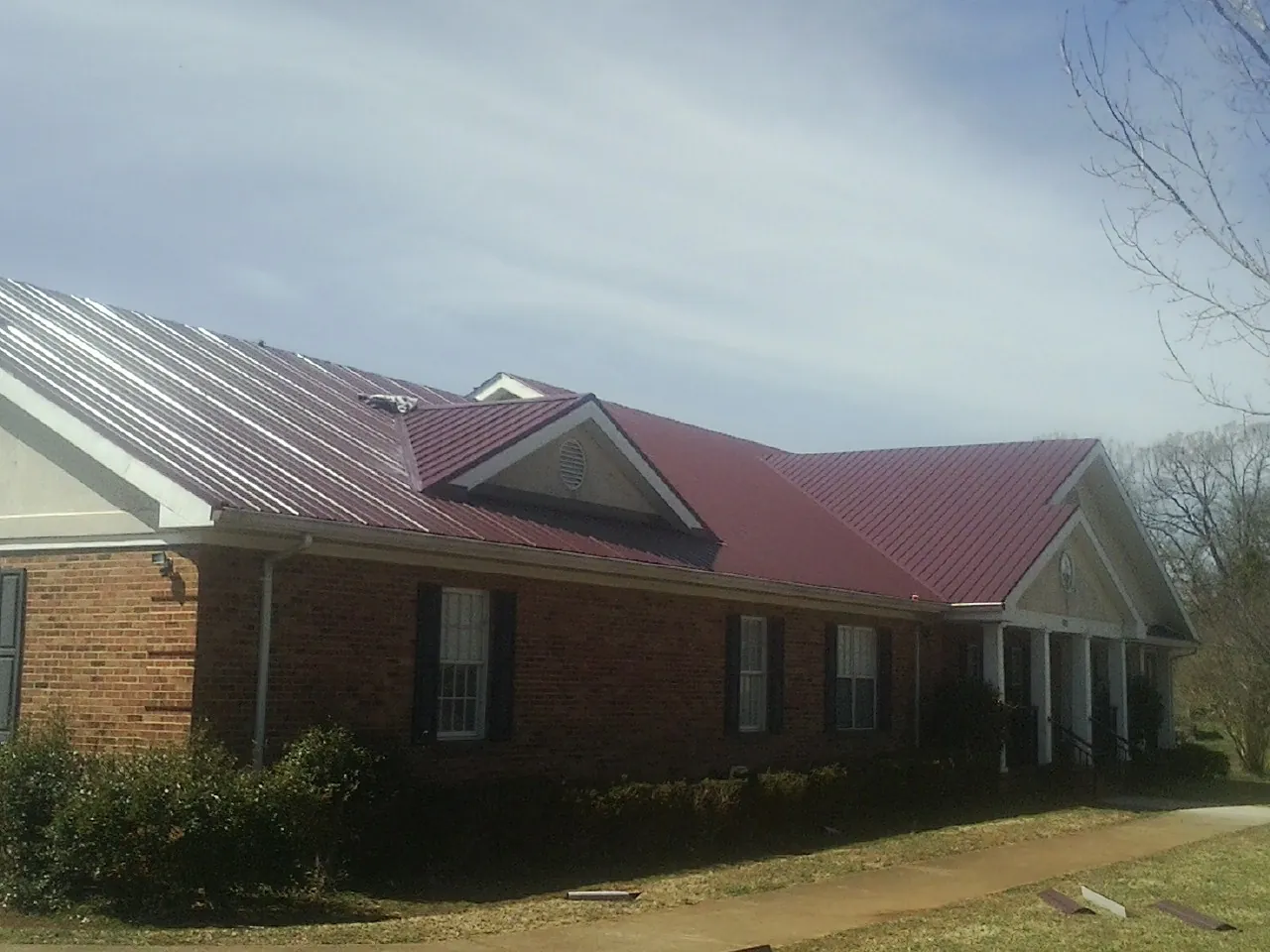 Red metal roof with gabled entries on a long brick building, from a Hail Damage Roof Repair job in La Vergne