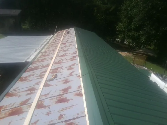 Old rusted panels beside newly installed green metal roofing — Wind Damage Roof Repair by Roofing Brothers in La Vergne