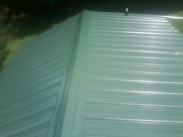 New green metal panels meeting at the ridge of a roof — Flat Roof Repair work by our crew in La Vergne