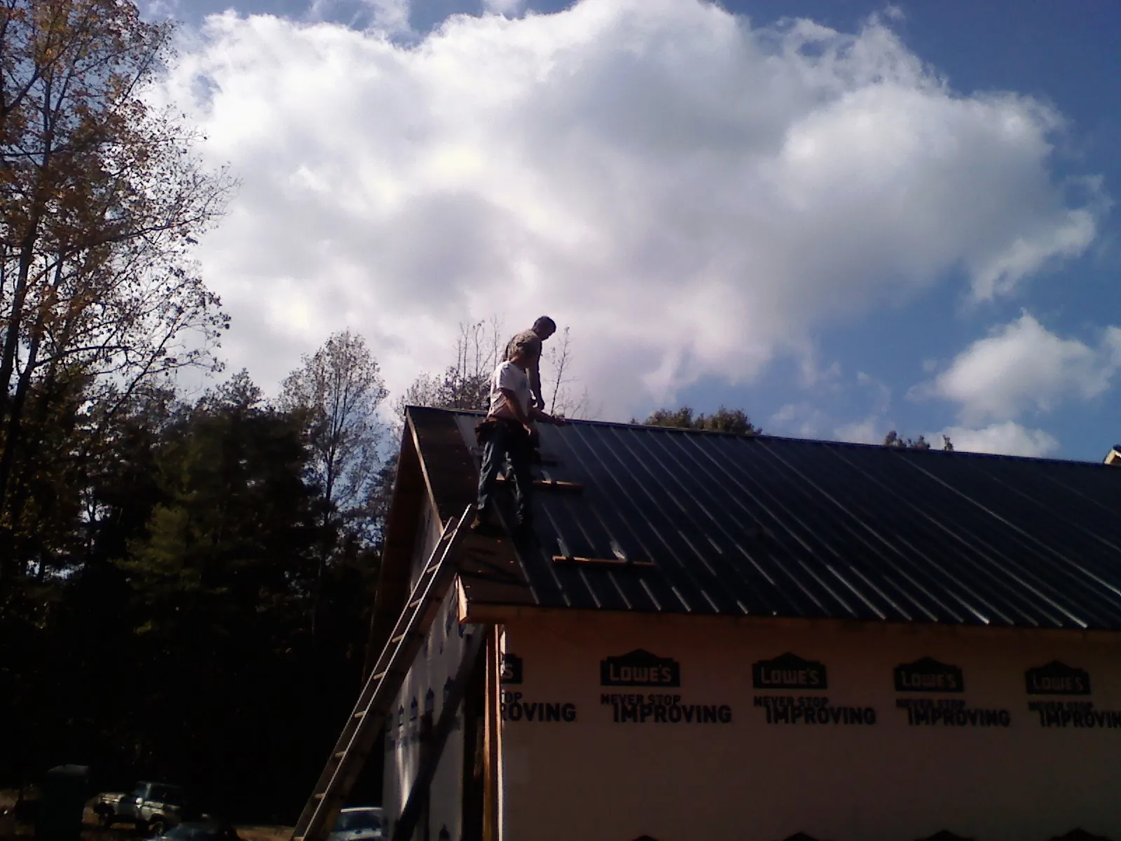 Roofer fastening dark metal panels high against a cloudy sky, from a Roof Inspection job in La Vergne