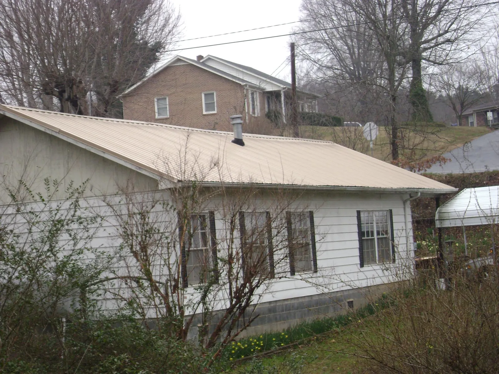 Tan metal roof on a white sided house set into a hillside — Commercial Roofing by Roofing Brothers in La Vergne